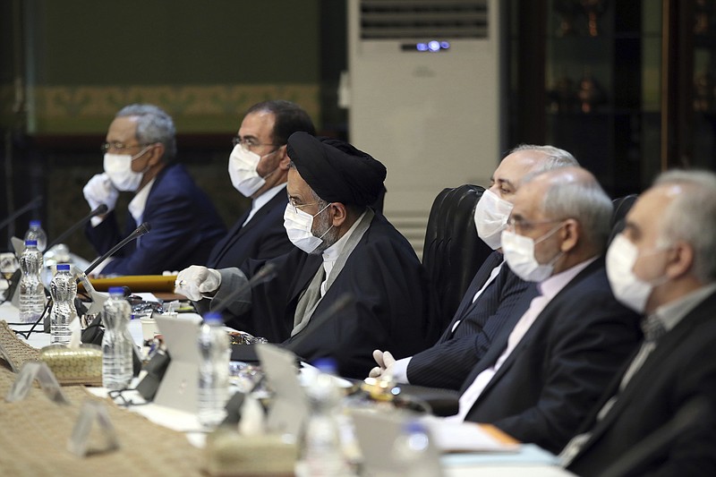 In this photo released by the official website of the Office of the Iranian Presidency, cabinet members wearing face masks and gloves attend their meeting in Tehran, Iran, Wednesday, March 18, 2020. For most people, the new coronavirus causes only mild or moderate symptoms. For some it can cause more severe illness. (Office of the Iranian Presidency via AP)