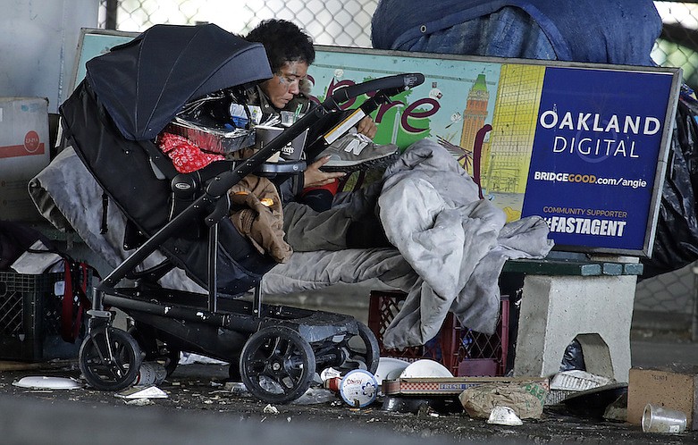 A homeless person holds a shoe while camped on a street bench Tuesday, March 17, 2020, in Oakland, Calif. Officials in seven San Francisco Bay Area counties have issued a shelter-in-place mandate affecting about 7 million people, including the city of San Francisco itself. The order says residents must stay inside and venture out only for necessities for three weeks starting Tuesday. (AP Photo/Ben Margot)