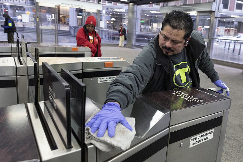 FILE - In this March 13, 2020 file photo, a worker disinfects a turnstile at the Government Center transit stop, in Boston. As the global viral pandemic grows, the need for cleaning and disinfecting has surged. Cleaners and domestic workers are essential in the effort to contain the virus. (AP Photo/Michael Dwyer, File)