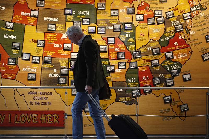 In this March 18, 2020 photo, a traveler checks his mobile telephone while passing a map of the United States on the way to the security checkpoint in the main terminal in Denver International Airport in Denver. Americans are increasingly worried they or a loved one will be infected by the coronavirus, with two-thirds now saying they're at least somewhat concerned — up from less than half who said so a month ago. That's according to a new poll from The Associated Press-NORC Center for Public Affairs Research that finds about 3 in 10 Americans say they're not worried at all. (AP Photo/David Zalubowski)