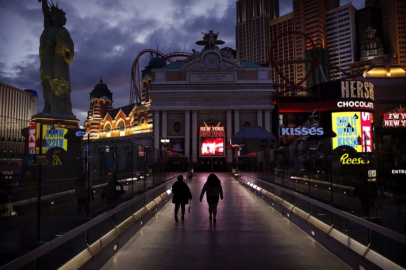 People walk along the Las Vegas Strip devoid of the usual crowds after casinos were ordered to shut down due to the coronavirus outbreak, March 18, 2020, in Las Vegas. (AP Photo/John Locher)

