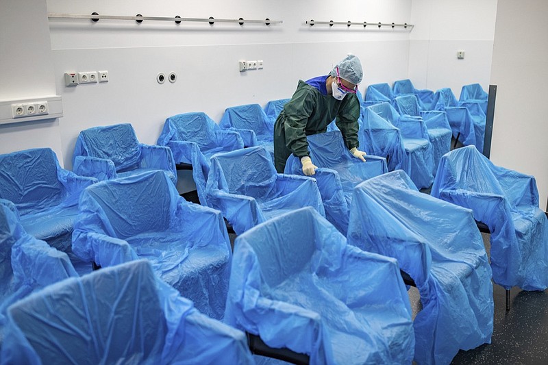 A nurse assembles plastic-wrapped chairs in a waiting area in the central emergency room of the University Hospital in Essen, Germany, Monday, March 23, 2020. The University Hospital in Essen has specially adapted to patients who have fallen ill with the coronavirus. (Marcel Kusch/dpa via AP)
