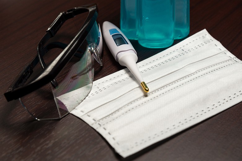 White Digital thermomether, Clear safety glasses, White face mask and Blue alcohol gel in a bottle on dark brown wooden background. Prevent the spread of germs and bacteria and avoid infections corona virus. / Getty Images/iStock/Prasith_To