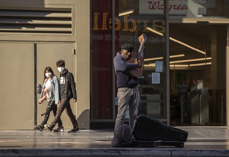 A lone street performer tunes his guitar on a mostly-empty Hollywood Boulevard in Los Angeles, Tuesday, March 24, 2020. New cases of the coronavirus surged around the state. (AP Photo/Damian Dovarganes)