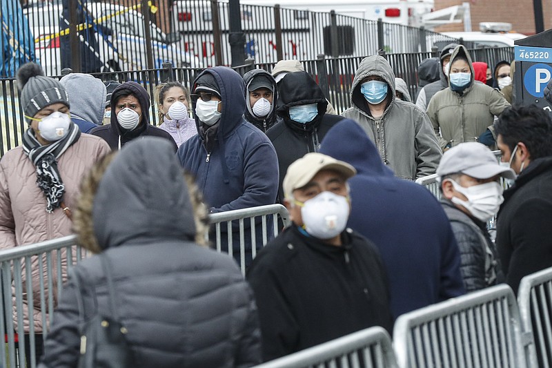 Photo by John Minchillo of The Associated Press / Patients wear personal protective equipment while maintaining social distancing as they wait in line for a COVID-19 test at Elmhurst Hospital Center on Wednesday, March 25, 2020, in New York.