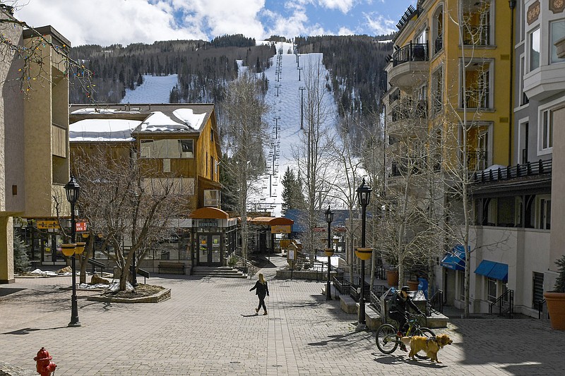 This Tuesday, March 24, 2020 photo shows people walking through empty streets at the base of Vail Ski Resort after the resort closed for the season amid the COVID-19 pandemic, in Vail, Colo. Ski resorts across the West that were shut down amid coronavirus fears are grappling with an economic blow at a time they would normally be welcoming hordes of spring break revelers. (AP Photo/Michael Ciaglo)


