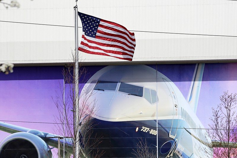 Photo by Elaine Thompson of The Associated Press / An American flag flutters in front of a Boeing airplane manufacturing plant, where murals of jets cover the massive doors on Monday, March 23, 2020, outside Seattle, in Renton, Washington.