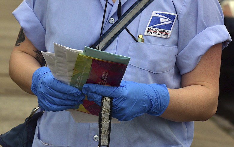 In this Friday March 20, 2020 file photo, a U.S Postal Service mail carrier wears gloves while delivering mail in South Wilkes-Barre, Pa. Health experts say the risks are very low that coronavirus will remain on envelopes or packages and infect anyone that comes in contact with it. But those on the frontlines of all those deliveries are taking steps to try to protect themselves. (Aimee Dilger/The Times Leader via AP)