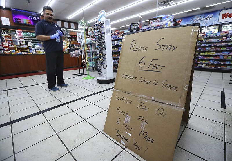 Ejaz Tarar stands next to his makeshift sign keeping customers six feet apart while cleaning the inside of the Food Mart in Newton County on Thursday, March 26, 2020, in Newborn. The store laid down tape to mark six foot barriers for customers. (Curtis Compton/Atlanta Journal-Constitution via AP)


