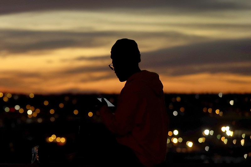 FILE - In this March 25, 2020, file photo, a person looks at a phone as the sun sets, in Kansas City, Mo. The city along with neighboring counties is under Stay at Home orders to help prevent the spread of COVID-19, the disease caused by the new coronavirus. (AP Photo/Charlie Riedel, File)