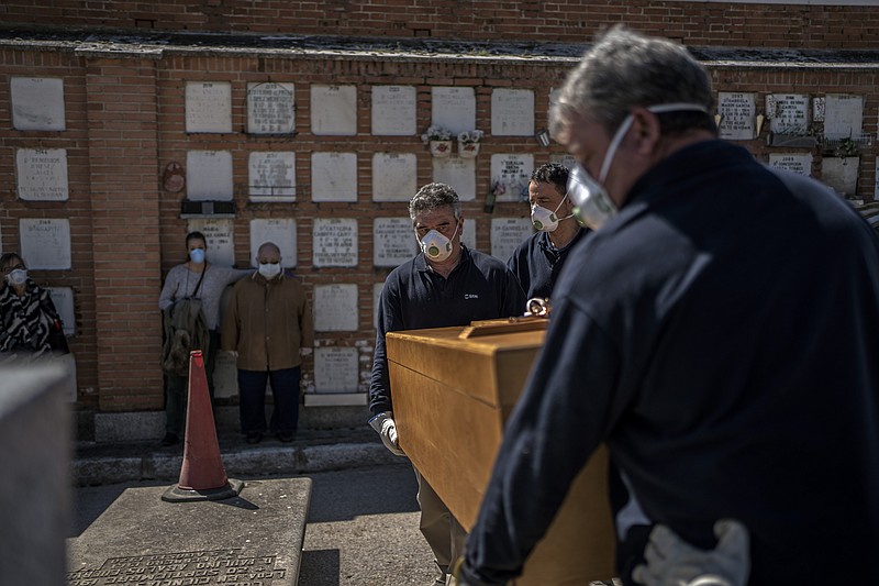 The daughter and husband, center left, no names available, of an elderly victim of the COVID-19 stand as undertakers place the coffin in the grave at the Almudena cemetery in Madrid, Spain, Saturday March 28, 2020. In Spain, where stay-at-home restrictions have been in place for nearly two weeks, the official number of deaths is increasing daily. The new coronavirus causes mild or moderate symptoms for most people, but for some, especially older adults and people with existing health problems, it can cause more severe illness or death. (AP Photo/Olmo Calvo)