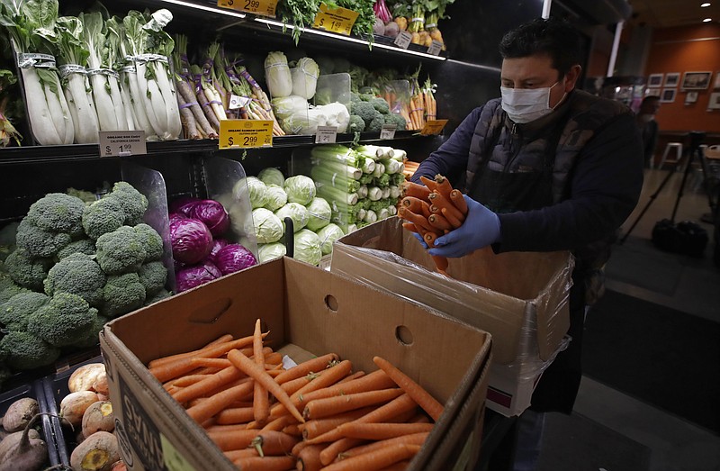 A worker, wearing a protective mask and gloves against the COVID-19 coronavirus, stocks produce before the opening of Gus's Community Market, Friday, March 27, 2020, in San Francisco. Health experts say there's no evidence the new coronavirus is spread through food. That's because organisms take different biological paths to sicken people. (AP Photo/Ben Margot)


