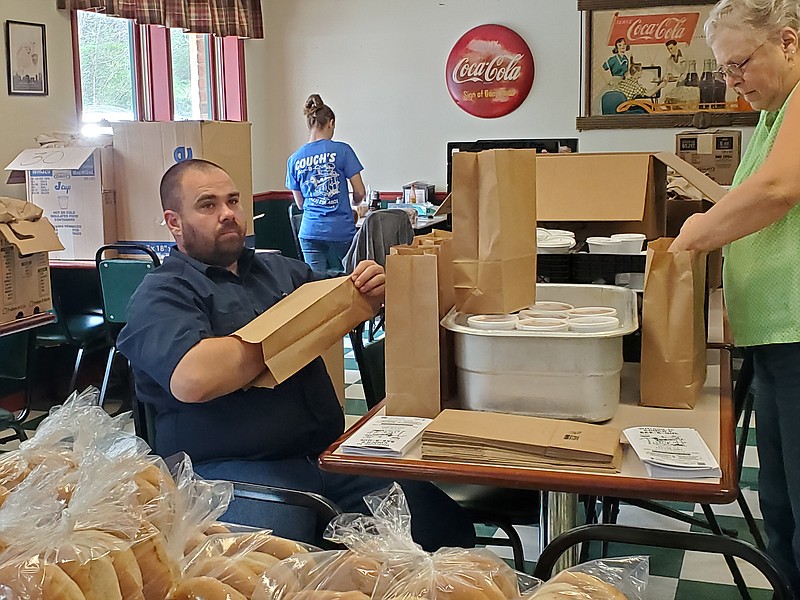 Photo from Sarah Johnson / Malcolm Johnson, left, and Valerie Stiner pack bags to fill Couch's recent order for 525 meals. In back, Christy Levi works on another part of the order.