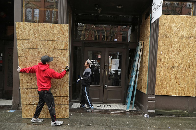 FILE - In this Monday, March 30, 2020 file photo, Phu Dang, left, the owner of i5 Pho restaurant, gets help from a contractor as he boards up his business in Seattle's downtown Pioneer Square neighborhood. Dang closed his business to dine-in customers earlier in the month and had tried doing takeout only food in response to the COVID-19 coronavirus pandemic, but he said his location did not attract enough customers for take out and he decided to fully close for the time being. He said his decision to board up came after a nearby business was broken into over the weekend. (AP Photo/Ted S. Warren)


