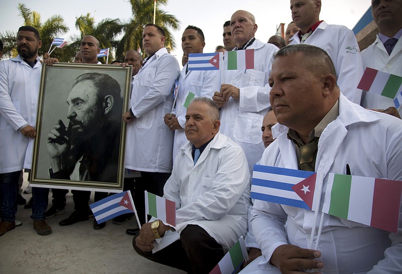 Several of the Cuban doctors and medical professionals that will depart for Italy to assist with the pandemic in the country pose for the media with a photo of Fidel Castro and flags of Italy and Cuba, in Havana, Cuba, Saturday, March 21, 2020. (AP Photo/Ismael Francisco)


