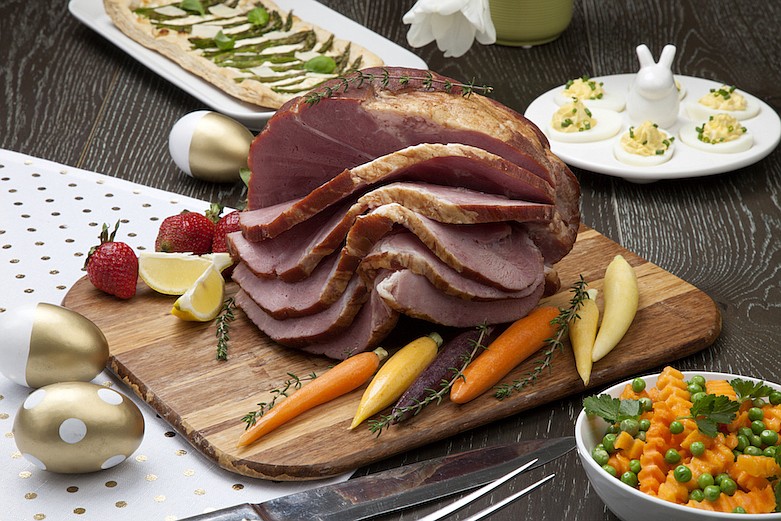 Roasted ham with deviled eggs, asparagus parmesan pastry, butternut squash with green peas, baby carrots, strawberries, and Easter decoration. / Getty Images/iStock/evgenyb