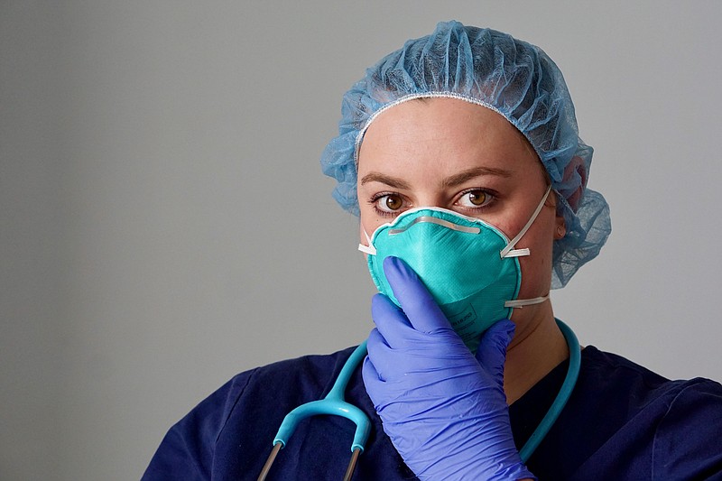 Close up of a female nurse putting on a respirator N95 mask to protect from airborne respiratory diseases such as the flu, coronavirus, ebola, TB, etc - stock photo ppe personal protective equipment tile / Getty Images
