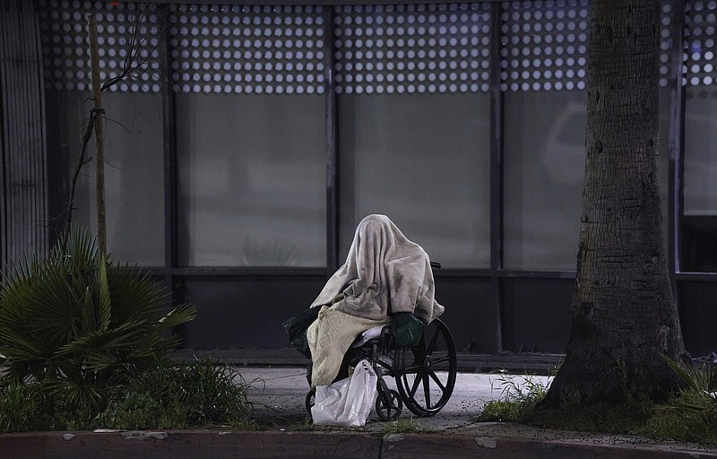 A homeless person sits on a wheelchair under rainy weather on Sunset Blvd., in the Echo Park neighborhood of Los Angeles Monday, April 6, 2020. One population is particularly vulnerable to contracting and spreading the coronavirus: the homeless. Officials have vowed repeatedly to get them indoors, but testing shortages and bureaucratic wrangling are making it difficult. Relatively few of California's 150,000 homeless population have been moved into individual quarters. It's unclear how many even have the highly contagious virus. It's a problem playing out nationwide and it's unclear how many may even have coronavirus. (AP Photo/Damian Dovarganes)


