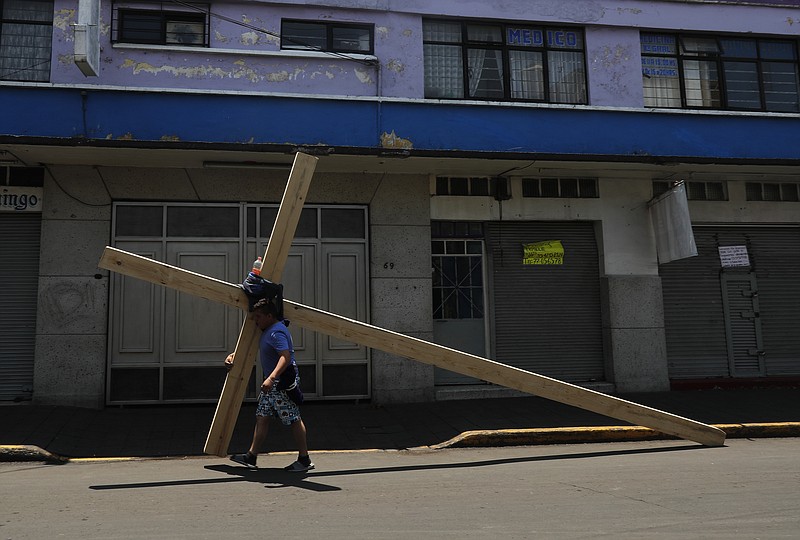 Alejandro Hernandez carries a cross to commemorate Jesus' crucifixion, through the popular neighborhood of Iztapalapa, in Mexico City, Friday, April 10, 2020, where police set up a barricade to keep faithful from gathering for the annual Way of the Cross reenactment. Christians are marking Good Friday in a world locked down by the COVID-19 pandemic, unable to attend solemn church services or religious processions as in past years. (AP Photo/Marco Ugarte)

