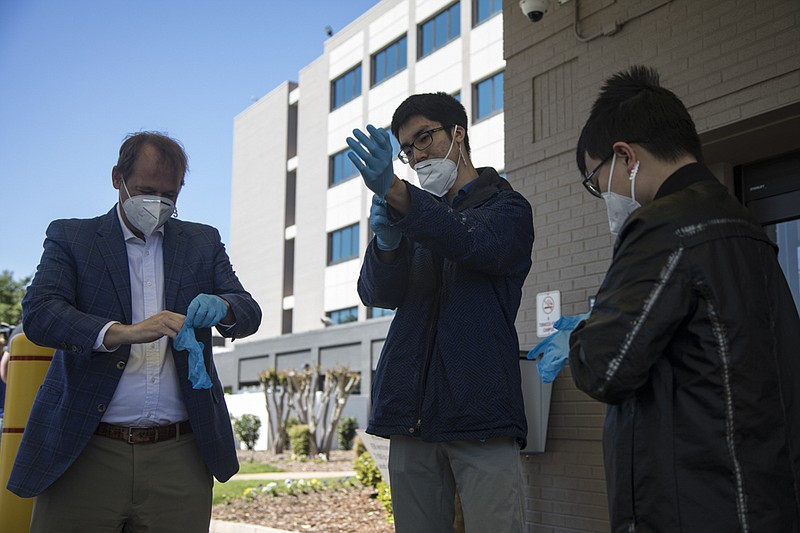 Staff photo by Troy Stolt / McCallie School Headmaster Lee burns, left, and McCallie seniors Jaden Long, center, and Derek Fu, right, both McCallie students from Shanghai, China, put on medical gloves at Parkridge Medical Center's main campus located at 2333 McCallie Ave. before donating over 2,000 face masks and n95 masks to the hospital on Friday, April 10, 2020 in Chattanooga, Tenn. The masks were donated by families of students from China who attend McCallie School.