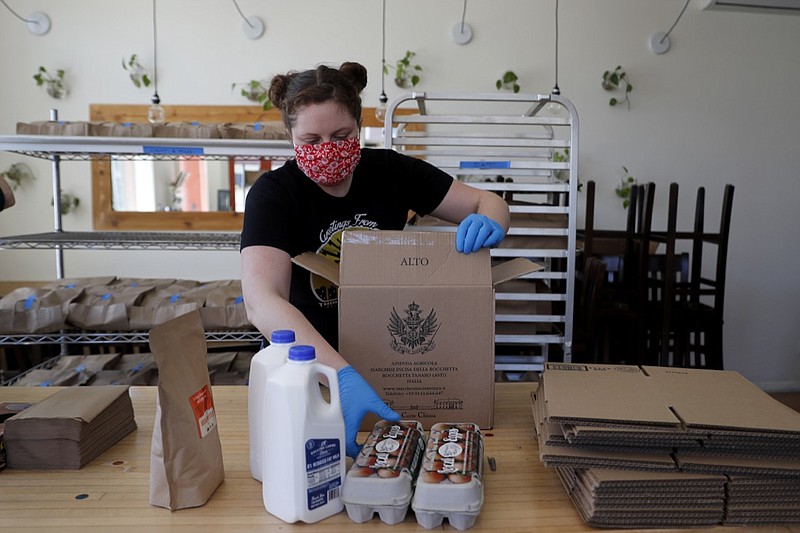 Monica Mileur packs grocery items into a box at Union Loafers restaurant Friday, April 10, 2020, in St. Louis. Some restaurants have turned to selling groceries and other provisions to customers as a way to help make up for revenue lost during the coronavirus outbreak. (AP Photo/Jeff Roberson)