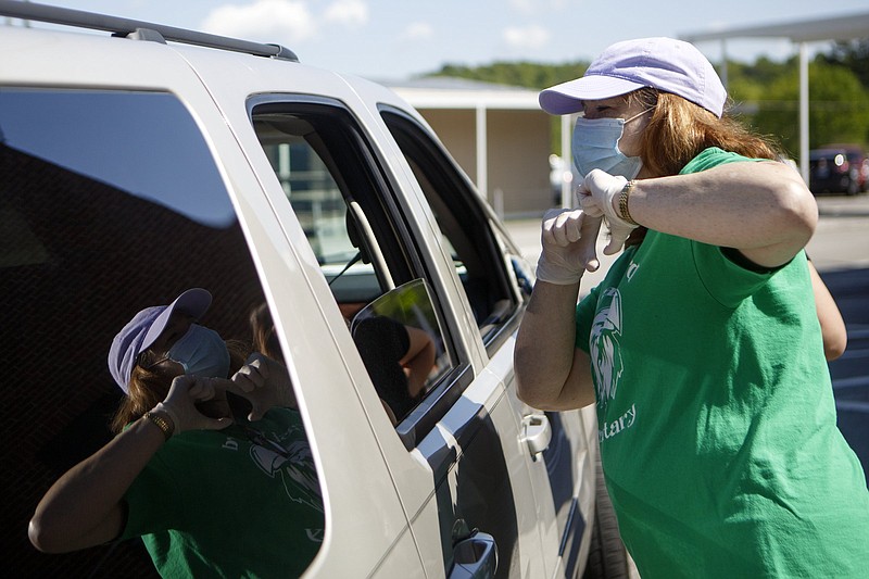 Staff photo by C.B. Schmelter / East Brainerd Elementary music teacher Lisa Steele makes a heart gesture as a family stops to pick up items at Chattanooga School for the Liberal Arts on Tuesday, April 21, 2020 in Chattanooga, Tenn. Teachers and volunteers made care packages for 250 East Brainerd Elementary students who were displaced by Easter Sunday's tornado. The packages included school materials but also items like Play-Doh, colored pencils and books.