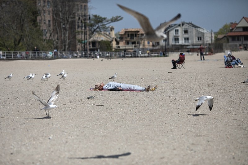 A woman sleeps on Brighton Beach in the Brooklyn borough of New York as seagulls flutter around her, on Saturday, April 25, 2020. With the weather warming up, more people wearing personal protective equipment are venturing out to the parks and streets, though most are still respecting the social distancing guidelines for the COVID-19 coronavirus. (AP Photo/Wong Maye-E)