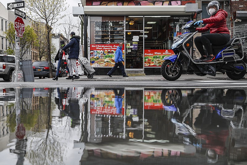 FILE - In this April 27, 2020, file photo, pedestrians and motorists wear personal protective equipment as they pass a small grocery that is one of the few businesses open on the street in New York. As some governors across the United States begin to ease restrictions imposed to stop the spread of the coronavirus, hopes are soaring that life as we knew it might be returning. But the plans emerging in many states indicate that "normal" is still a long way off. (AP Photo/John Minchillo, File)


