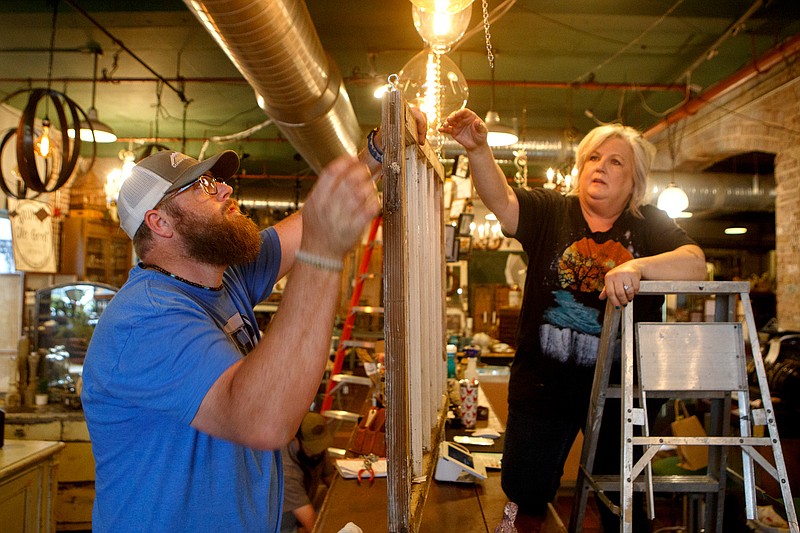 Staff photo by C.B. Schmelter / Owner Carol Ellis, right, and Chris Rogers hang a window between the register and the retail floor at The Refindery on Wednesday, April 29, 2020 in Chattanooga, Tenn. Following the shutdown due to the coronavirus pandemic, the store is preparing to reopen on Friday, May 1.