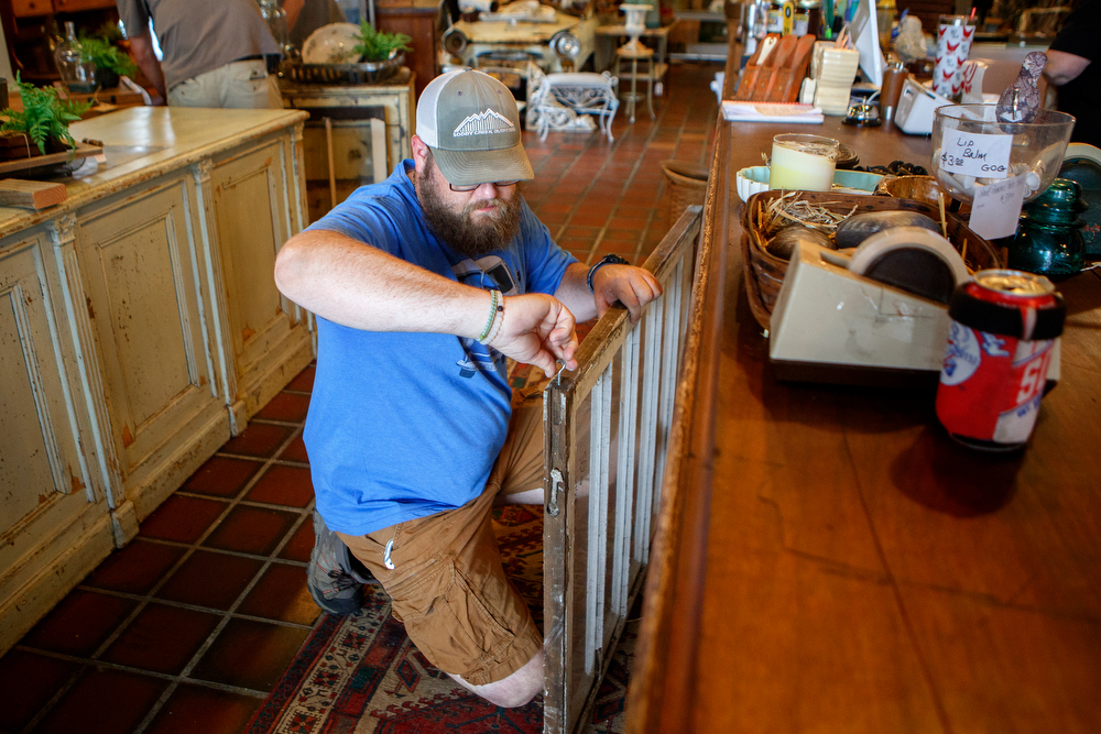 Staff photo by C.B. Schmelter / Chris Rogers inserts a screw hook into a window to create a barrier between the counter and retail floor at The Refindery on Wednesday, April 29, 2020 in Chattanooga, Tenn. Following the shutdown due to the coronavirus pandemic, the store is preparing to reopen on Friday, May 1.
