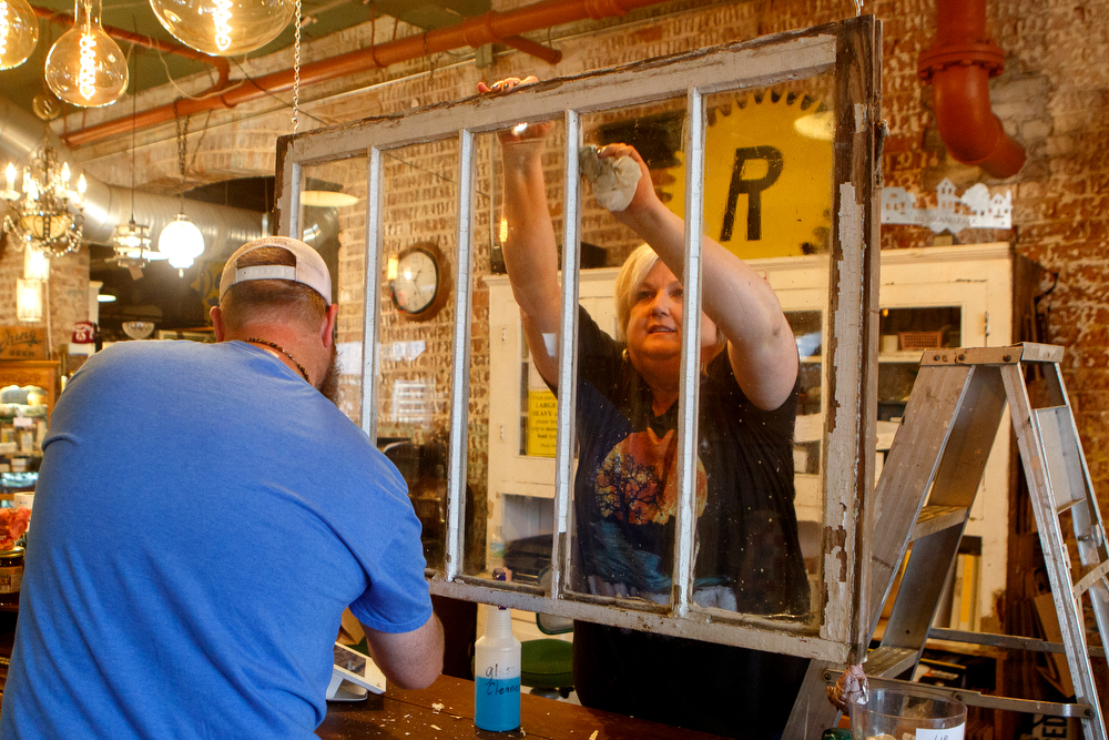 Staff photo by C.B. Schmelter / Owner Carol Ellis, right, and Chris Rogers work on cleaning up after hanging a window between the register and the retail floor at The Refindery on Wednesday, April 29, 2020 in Chattanooga, Tenn. Following the shutdown due to the coronavirus pandemic, the store is preparing to reopen on Friday, May 1.
