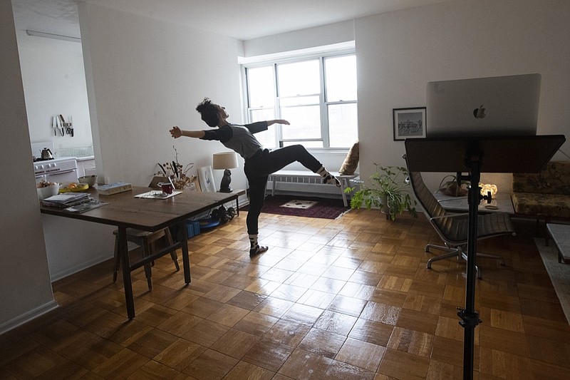 In this Thursday, April 23, 2020, photo dancer and choreographer Netta Yerushalmy warms up during a zoom dance rehearsal in her living room on the Lower East Side neighborhood of New York. Yerushalmy has built a career in movement and community. Both are gone now. Across the city, the coronavirus pandemic has upended almost everyone's lives, but the arts community — the dancers, actors, visual artists and designers, who never made much income to start with — is especially suffering, imperiling New York City as a creative capital. (AP Photo/Mary Altaffer)