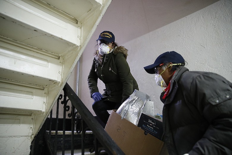 Sandra Perez, left, and Francisco Ramírez, carry a box of donated groceries to a family in need, Saturday, April 18, 2020, in the Queens borough of New York. Some are former construction workers or cleaning ladies who lost their jobs and can barely pay rent, but they go out each day to deliver donated diapers, formula or food to families in need. (AP Photo/John Minchillo)