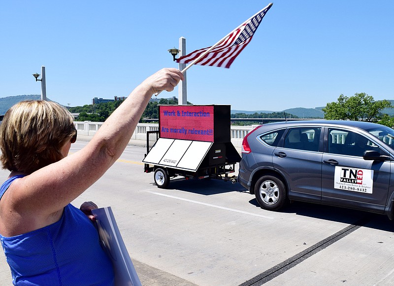 Staff Photo by Robin Rudd / Sharon Sessoms, of Chattanooga, waves her flag as a fellow protestor pulls a electronic sign with a favorable message, "Work and interaction are morally relevant."   The Reopen Chattanooga, honk your horn protest in downtown Chattanooga on May 2, 2020.  