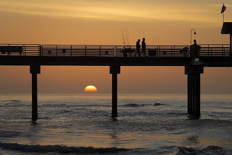 People walk on a pier with their fishing poles during sunrise on the Gulf of Mexico, in Orange Beach, Ala., Friday, March 13, 2020. (AP Photo/Gerald Herbert)