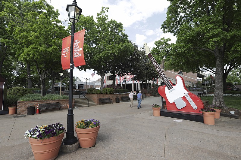 In this Wednesday, April 28, 2020, photo, two people walk through the otherwise deserted plaza outside the Grand Ole Opry House in Nashville, Tenn. The Opry has suspended all events through May 16 due to the coronavirus pandemic. As businesses start to gradually reopen across the state, Tennessee tourism destinations like the Grand Ole Opry, Graceland and Dollywood remain closed. But many of them are preparing to start welcoming visitors once again in a state where tourists spent $22 billion in 2018. (AP Photo/Mark Humphrey)