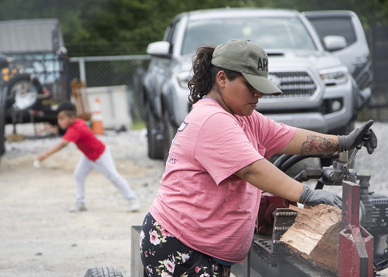 Staff photo by Troy Stolt / Lola Perez splits wood as her son Romeo, 7, plays behind her at Garcia Tree Service on 37th street on Thursday, May 14, 2020 in Chattanooga, Tenn. Approximately one in five cases of coronavirus in Hamilton County have come from the 37407 zip code, which includes the East Lake and Clifton Hills neighborhoods, though the area only makes up three percent of the County's population.