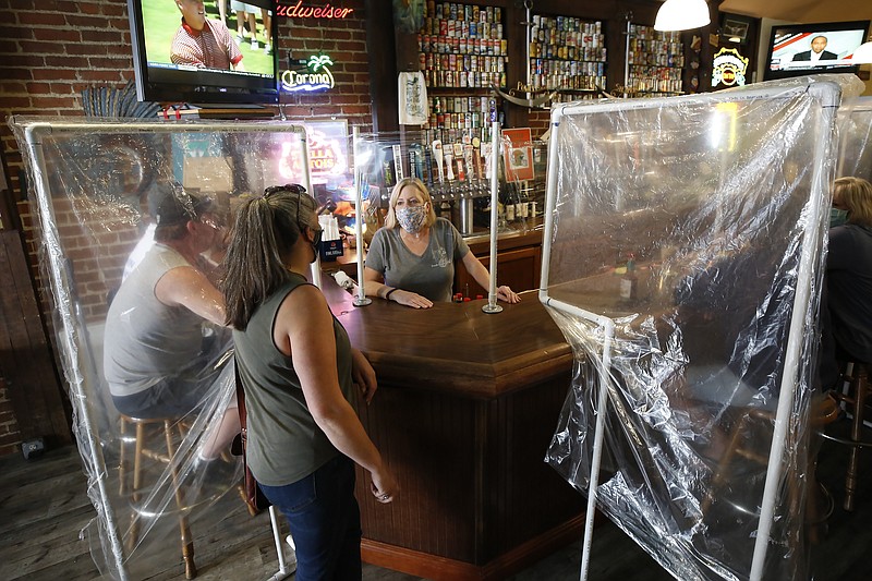 FILE - In this Wednesday, May 13, 2020 file photo, Sheila Kelly, owner of Powell's Steamer Co. & Pub, center, stands behind makeshift barriers as she helps patrons at her restaurant in the El Dorado County town of Placerville, Calif. It was the first day Kelly was serving in-dining meals since the state's lockdown order to slow the spread of the coronavirus. El Dorado County was one of the first counties to win approval from the state to reopen for dining-in. (AP Photo/Rich Pedroncelli)


