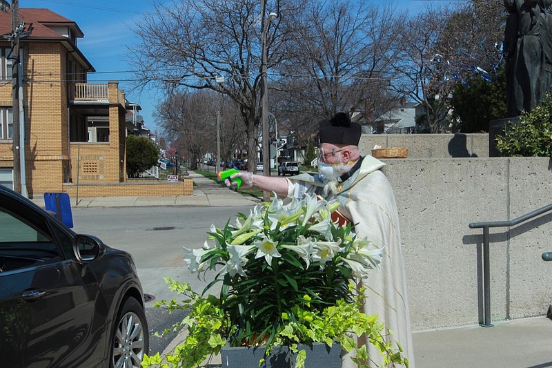 FILE - In this Saturday, April 11, 2020 file photo, Rev. Timothy Pelc blesses Easter baskets outside St. Ambrose Church in Grosse Pointe Park, Mich. Pelc, wearing church vestments and protective gear, offered a prayer and sprayed holy water from a squirt gun instead of blessing baskets inside the church in a bid to maintain social distancing during the coronavirus pandemic. (Natalie White via AP)
