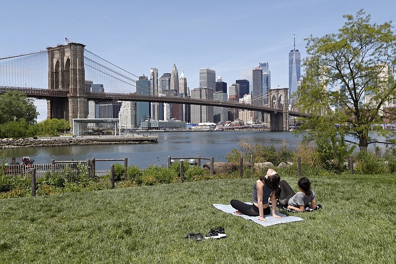 Two women, neither of whom were wearing protective face coverings, sunbathe on a grassy slope at Brooklyn Bridge Park during the current coronavirus outbreak, Sunday, May 17, 2020, in New York. (AP Photo/Kathy Willens)