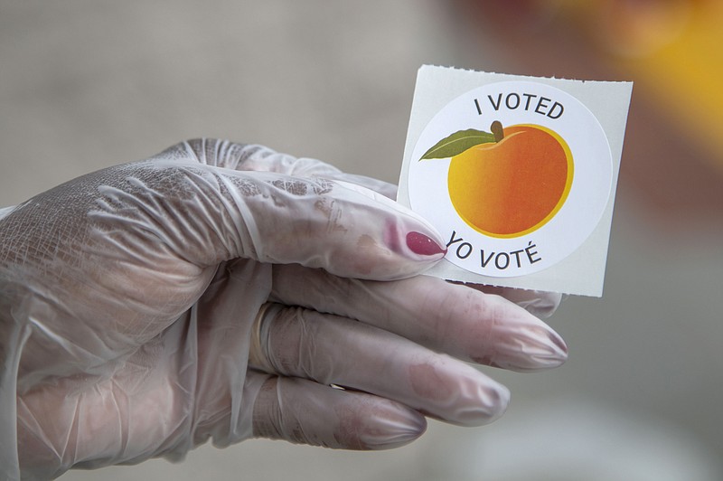 An early voter, who wore gloves to cast their ballot, shows off their sticker during Georgia's primary election at the Gwinnett County Voter Registration and Elections Office in Lawrenceville, Ga., Monday, May 18, 2020. Early voting began Monday and will last three-weeks. Georgia's Election Day is Tuesday, June 9.  (Alyssa Pointer/Atlanta Journal-Constitution via AP)