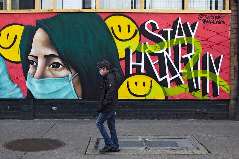 File photo by Ruth Fremson of The New York Times / A pedestrian with a face mask walks past a mural in Seattle, Washington, on May 5, 2020.