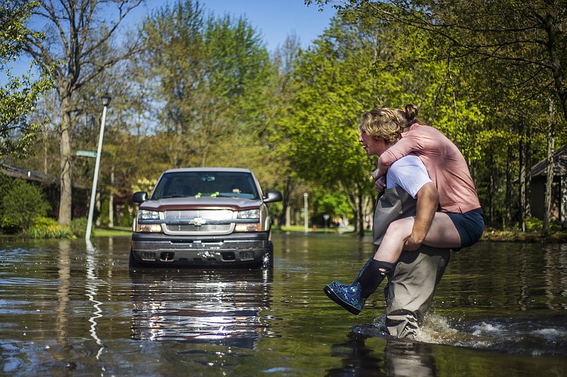 Ryan Stadelmaier, 16, gives a piggyback ride to his sister Rachel Stadelmaier, 27, as they cross Walden Woods Drive while helping residents tend to their flooded homes, Wednesday, May 20, 2020, in Midland, Mich. (Katy Kildee/Midland Daily News via AP)