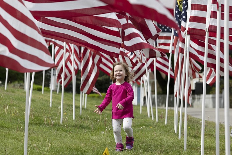 Hazel Roberts walks in a field of flags ahead of Memorial Day, Saturday, May 23, 2020, in Cohasset, Mass. (AP Photo/Michael Dwyer)