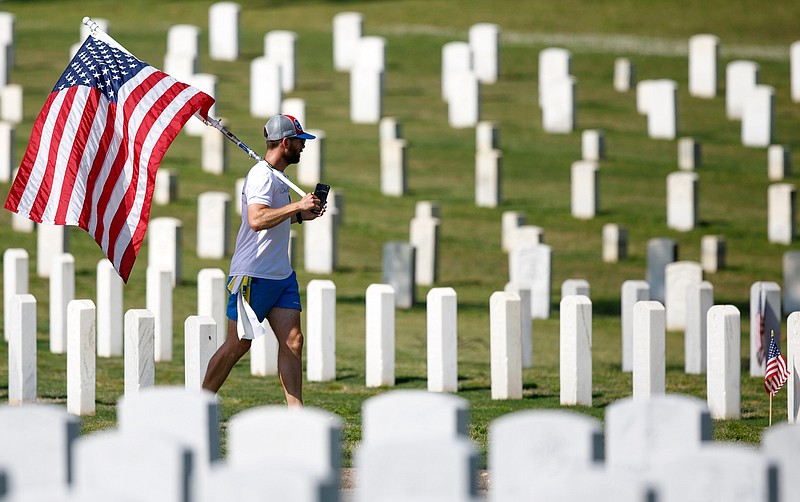 Staff photo by C.B. Schmelter / Veteran Russell Larkins runs with an American flag on Memorial Day at the Chattanooga National Cemetery on Monday, May 25, 2020 in Chattanooga, Tenn. Larkins is currently raising money for veterans affected by COVID-19 by running from North Carolina to California.