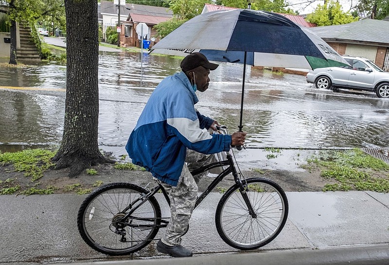 A man rides a bicycle while holding an umbrella as rain from Tropical Storm Bertha flooded a few streets in Charleston, S.C., Wednesday, May 27, 2020. (Matthew Fortner/The Post And Courier via AP)