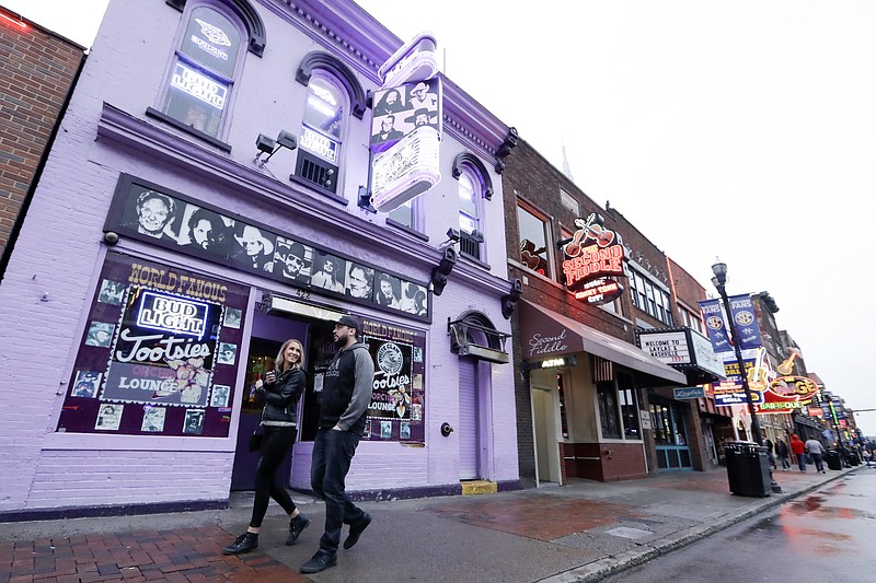 People walk by Tootsie's Orchid Lounge, closed because of the coronavirus, Monday, March 16, 2020, in Nashville, Tenn. Nashville Mayor John Cooper has called for bars on Broadway and throughout the county to close until further notice. He also asked restaurants to limit seating to 50 percent of capacity, with a cap of 100 people, and restaurant bars to not allow standing. (AP Photo/Mark Humphrey)