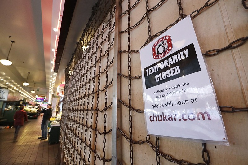 FILE - In this Thursday, April 2, 2020 file photo a sign explains the closure of a shop in the Pike Place Market in Seattle. As the coronavirus outbreak has caused record number of people to seek unemployment benefits Washington state officials said Thursday that impostors have used the stolen information of tens of thousands of people to receive hundreds of millions of dollars in unemployment benefits. (AP Photo/Elaine Thompson,File)