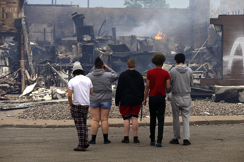 Onlookers watch as smoke smolders from a destroyed fast food restaurant near the Minneapolis Police Third Precinct, Thursday, May 28, 2020, after a night of rioting and looting as protests continue over the death of George Floyd, who died in police custody Monday night in Minneapolis after video shared online by a bystander showed a white officer kneeling on his neck during his arrest as he pleaded that he couldn't breathe. (AP Photo/Jim Mone)
