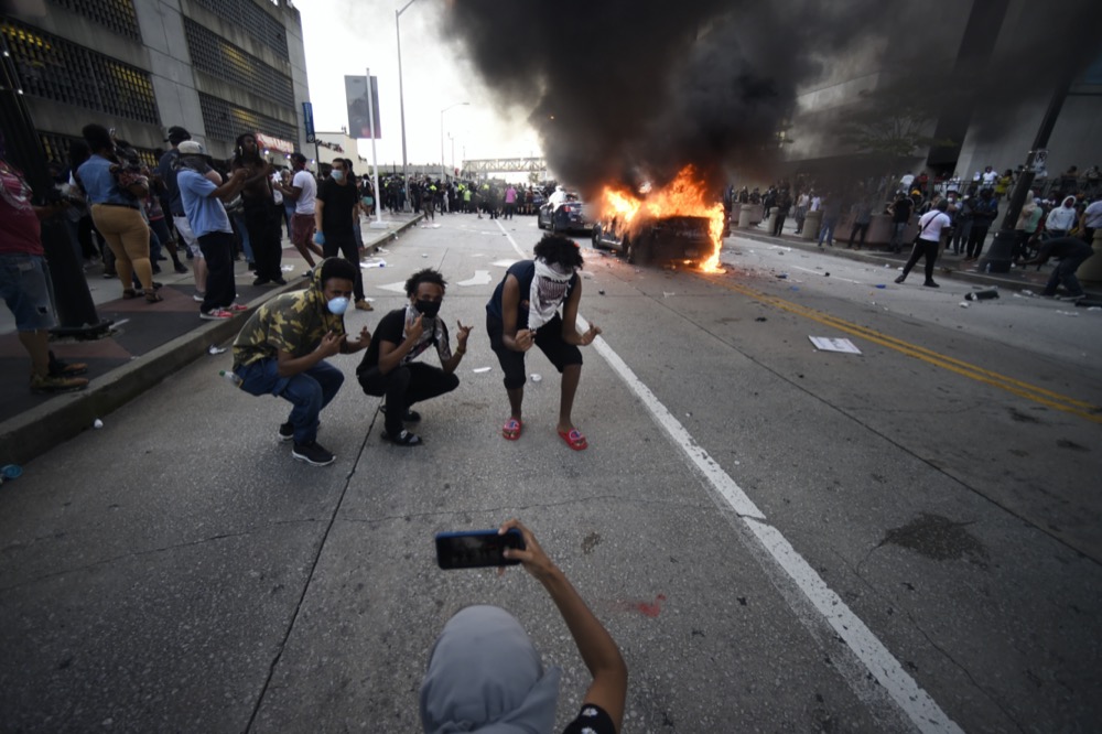 An Atlanta Police Department vehicle burns as people pose for a photo during a demonstration against police violence, Friday, May 29, 2020, in Atlanta. The protest started peacefully earlier in the day before demonstrators clashed with police. The Memorial Day death of George Floyd in police custody in Minneapolis has sparked protests nationwide. (AP Photo/Mike Stewart)